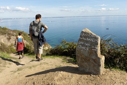 Un couple de randonneurs empruntant un des nombreux sentiers côtiers de l' ile de Groix. Un rocher dressé tel un menhir est utilisé comme panneau indicateur.A couple of hikers along one of the many coastal paths of the island of Groix. A rock stands as a menhir is used as a sign.