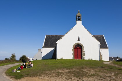 Ile de Groix _ Une famille, assise sur l' herbe, pique-nique devant la Chapelle de Quelhuit par une belle journée d' été _Island of Groix _ A family sitting on the grass, picnic at the Chapel of Quelhuit on a beautiful summer day
