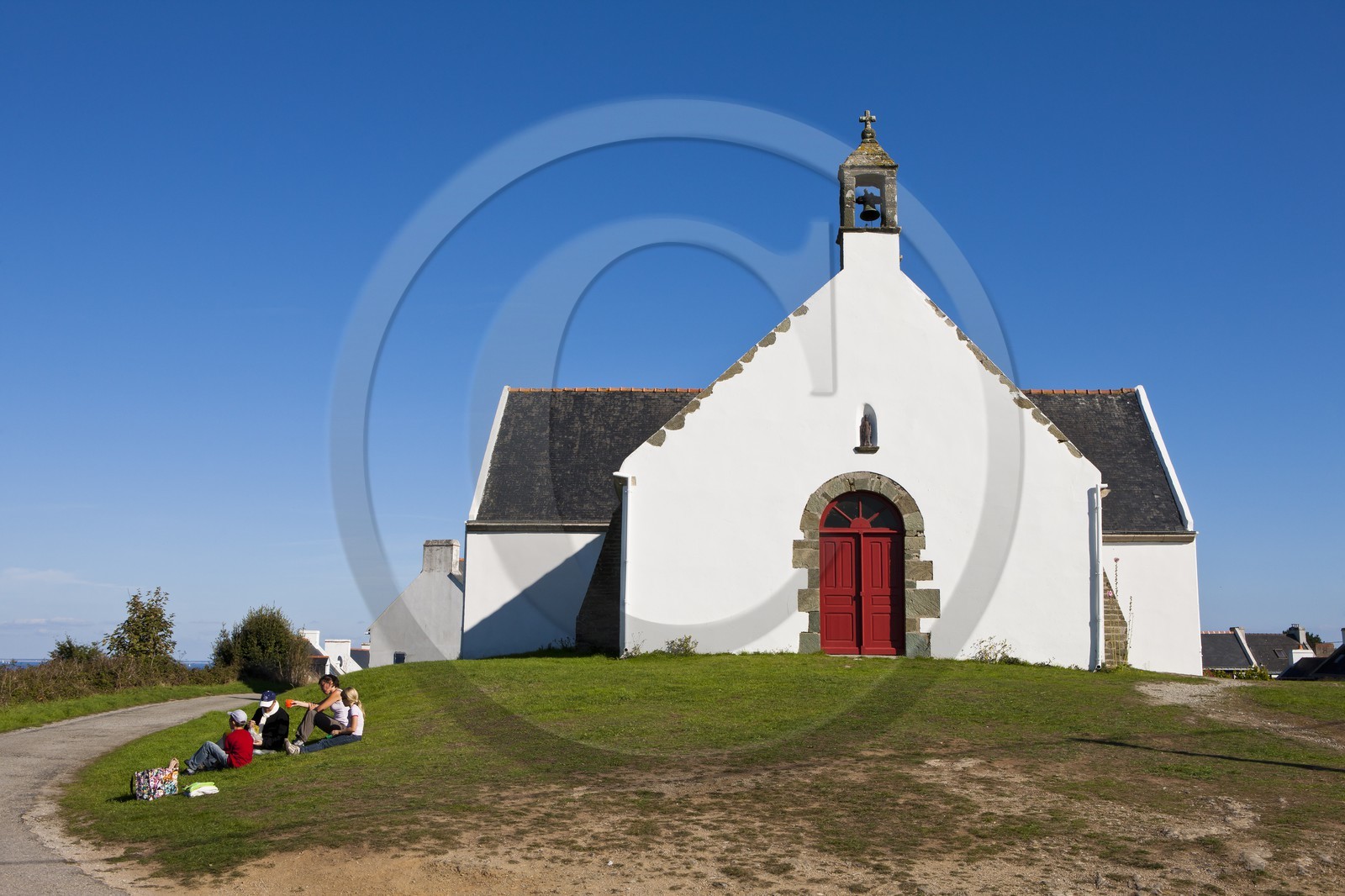 Ile de Groix _ Une famille, assise sur l' herbe, pique-nique devant la Chapelle de Quelhuit par une belle journée d' été _Island of Groix _ A family sitting on the grass, picnic at the Chapel of Quelhuit on a beautiful summer day