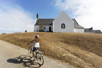 Une jeune fille à vélo passe devant la Chapelle de Quelhuit sur l' Ile de Groix.A young girl riding a bike in front of the Chapel of Quelhuit on the Ile de Groix.